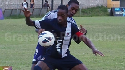 JC’s Captain Junior Flemmings shield off Kingston College defender Romar Beckford.